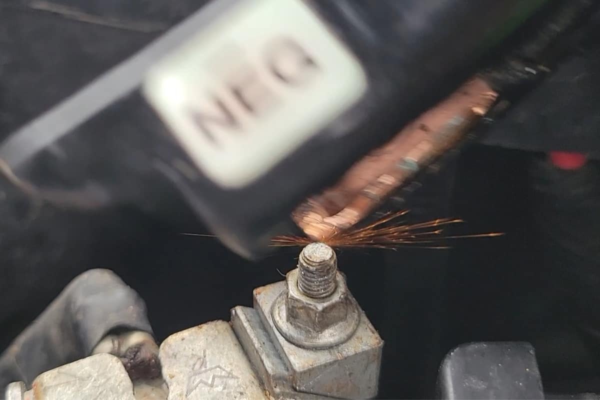 up close Image showing a set of jumper cables causing a spark when connected to a dead car battery.